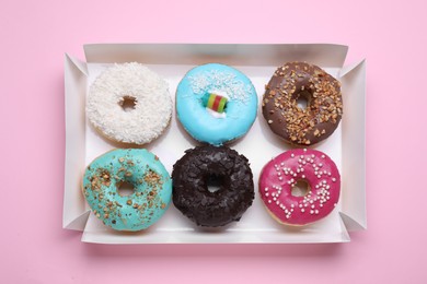 Photo of Box with different tasty glazed donuts on pink background, top view