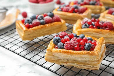 Photo of Cooling rack and fresh delicious puff pastry with sweet berries on white marble table, closeup