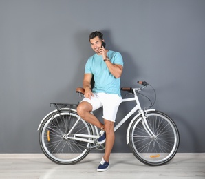 Photo of Handsome young hipster man with bicycle and phone near color wall