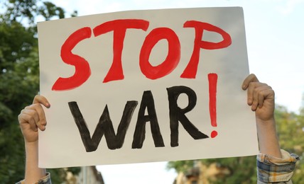 Photo of Woman holding poster with words Stop War outdoors, closeup