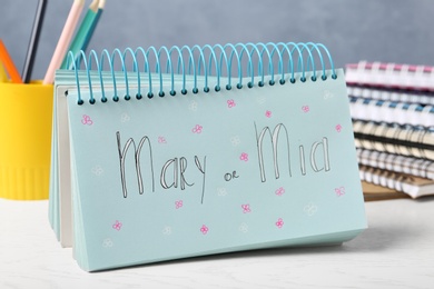 Photo of Notebook with written baby names and stationery on white wooden table
