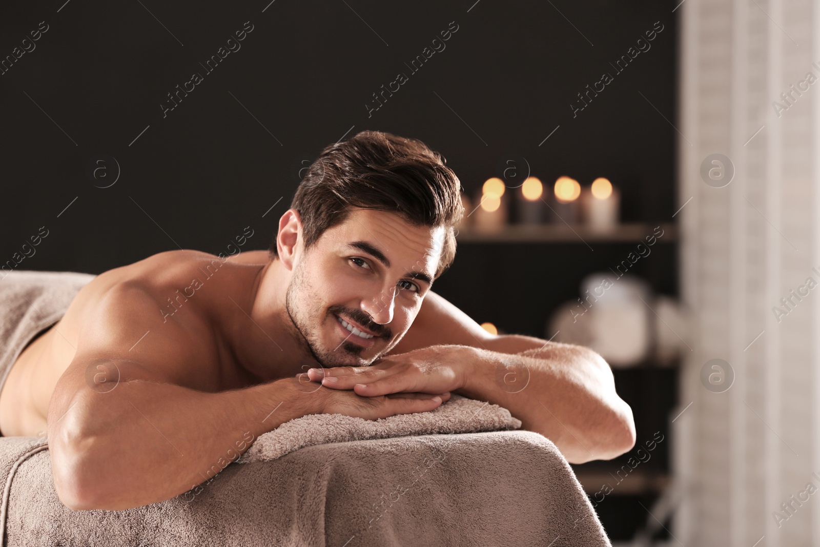 Photo of Handsome young man relaxing on massage table in spa salon, space for text