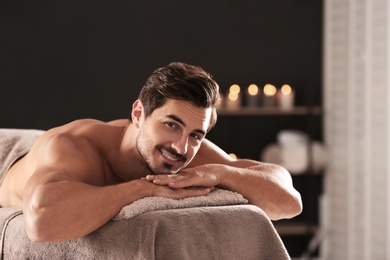 Photo of Handsome young man relaxing on massage table in spa salon, space for text