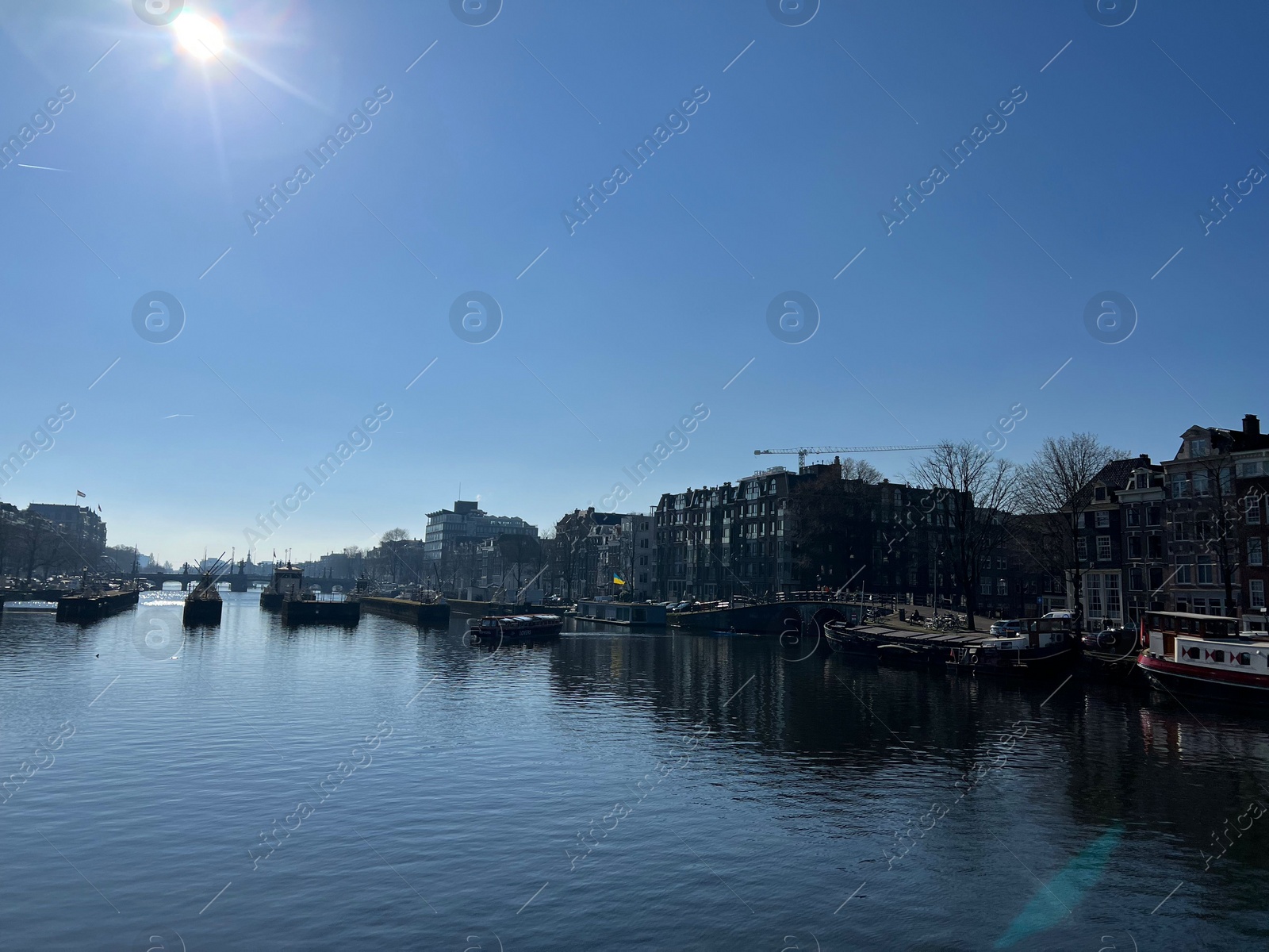 Photo of Amsterdam, Netherlands - March 01, 2023: Picturesque view of river embankment with moored boats in city under blue sky