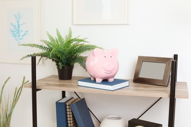 Photo of Shelving unit with decorative interior elements and piggy bank near white wall