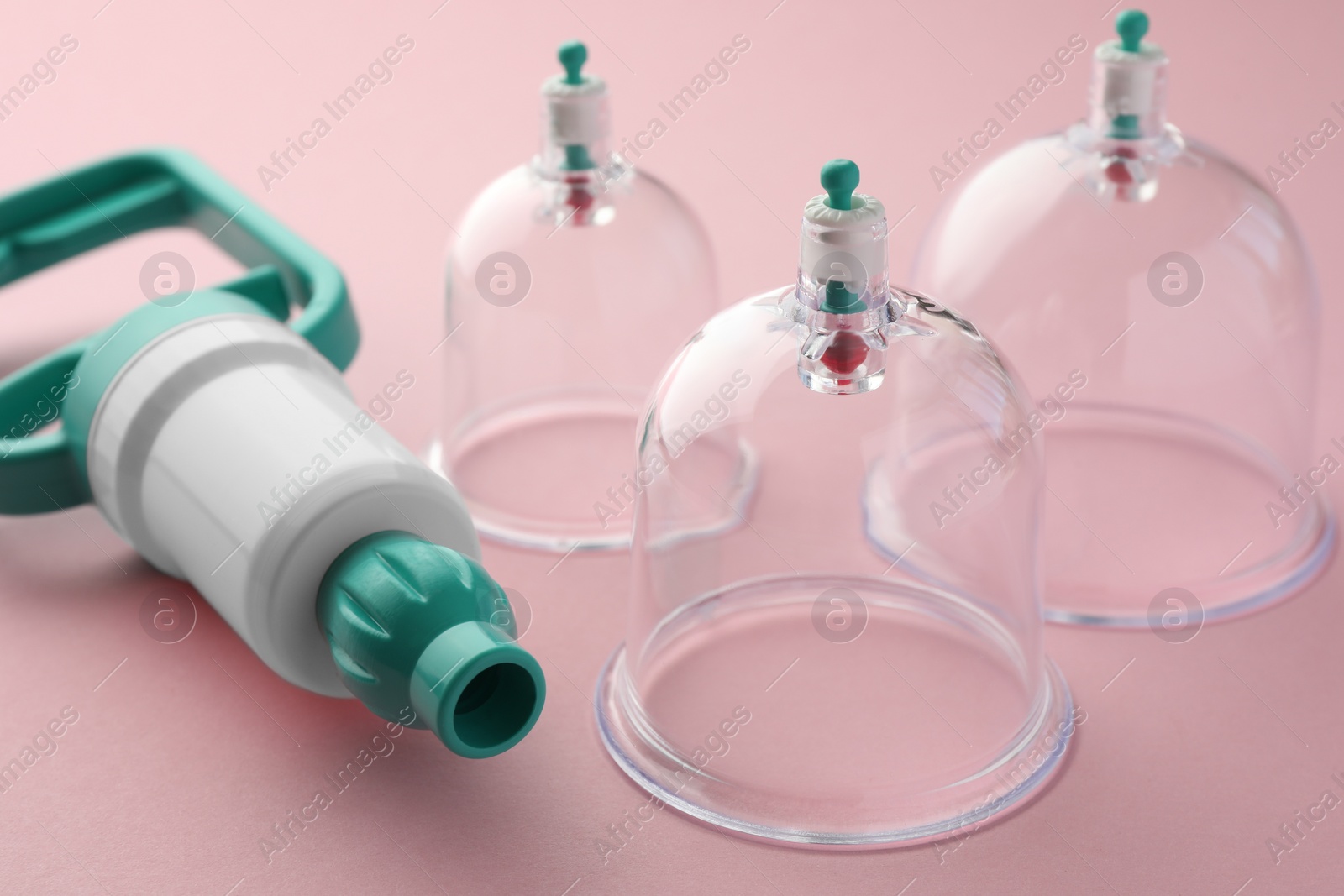 Photo of Plastic cups and hand pump on pink background, closeup. Cupping therapy