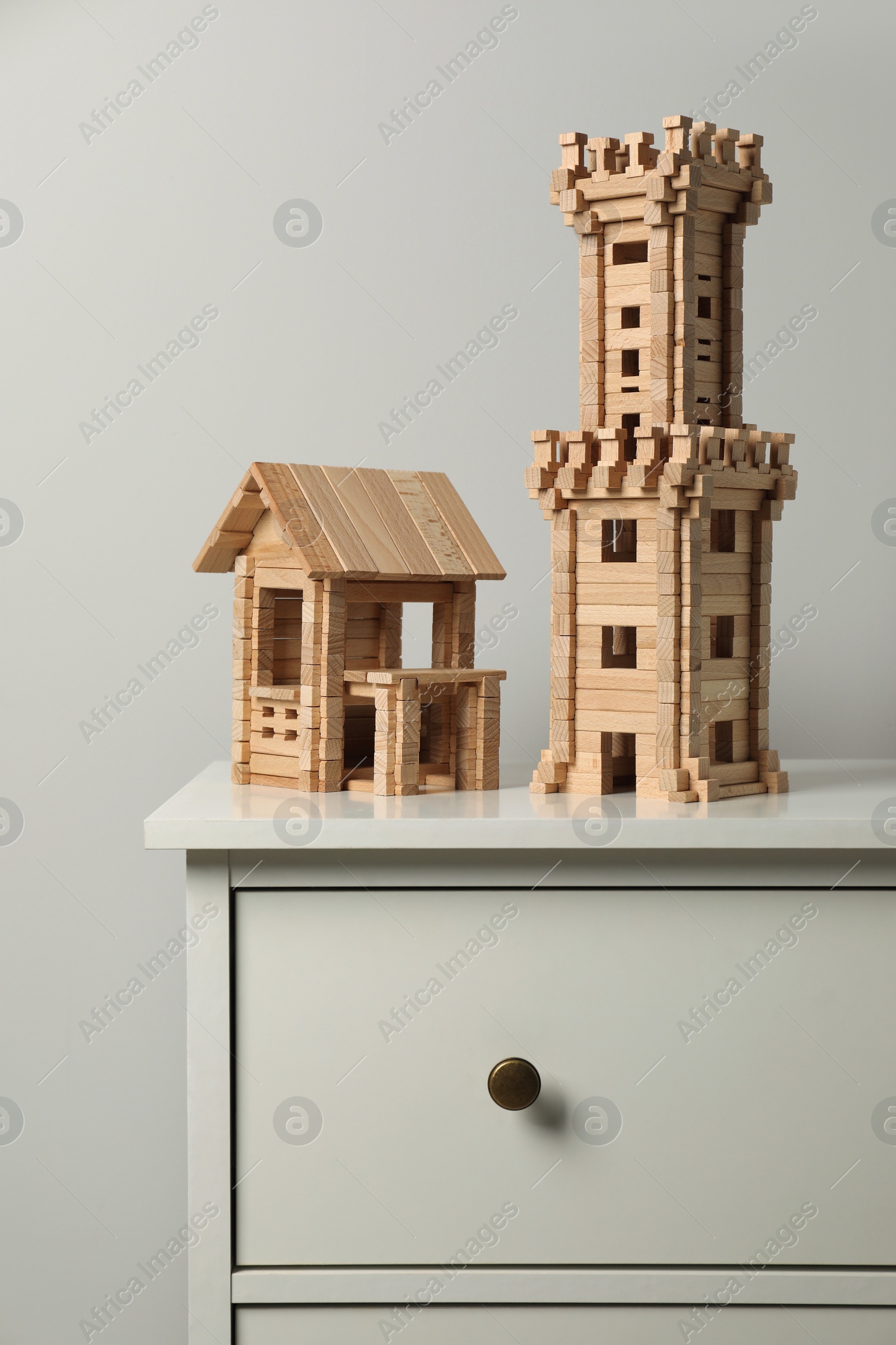 Photo of Wooden tower and house on chest of drawers near light grey wall. Children's toys