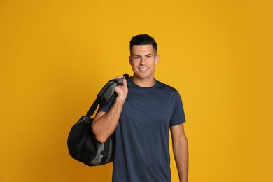 Handsome man with sports bag on yellow background