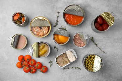 Photo of Open tin cans with different preserved products on grey table, flat lay