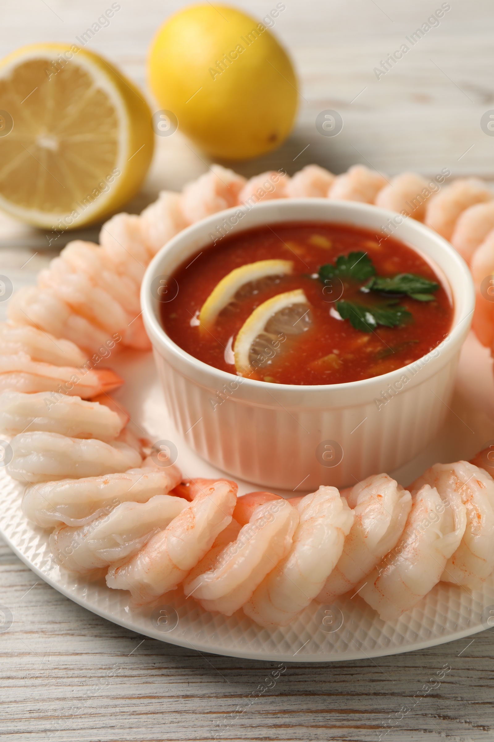 Photo of Tasty boiled shrimps with cocktail sauce and lemon on white wooden table, closeup