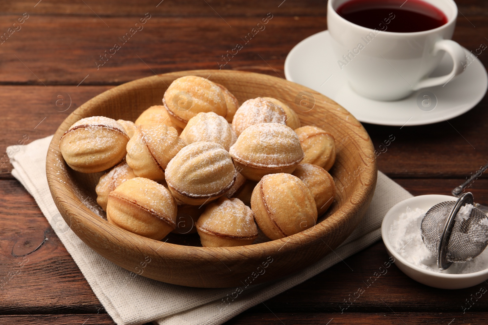 Photo of Delicious nut shaped cookies with boiled condensed milk and powdered sugar on wooden table
