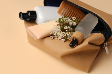 Photo of Preparation for spa. Compact toiletry bag with different cosmetic products and flowers on light brown background, closeup