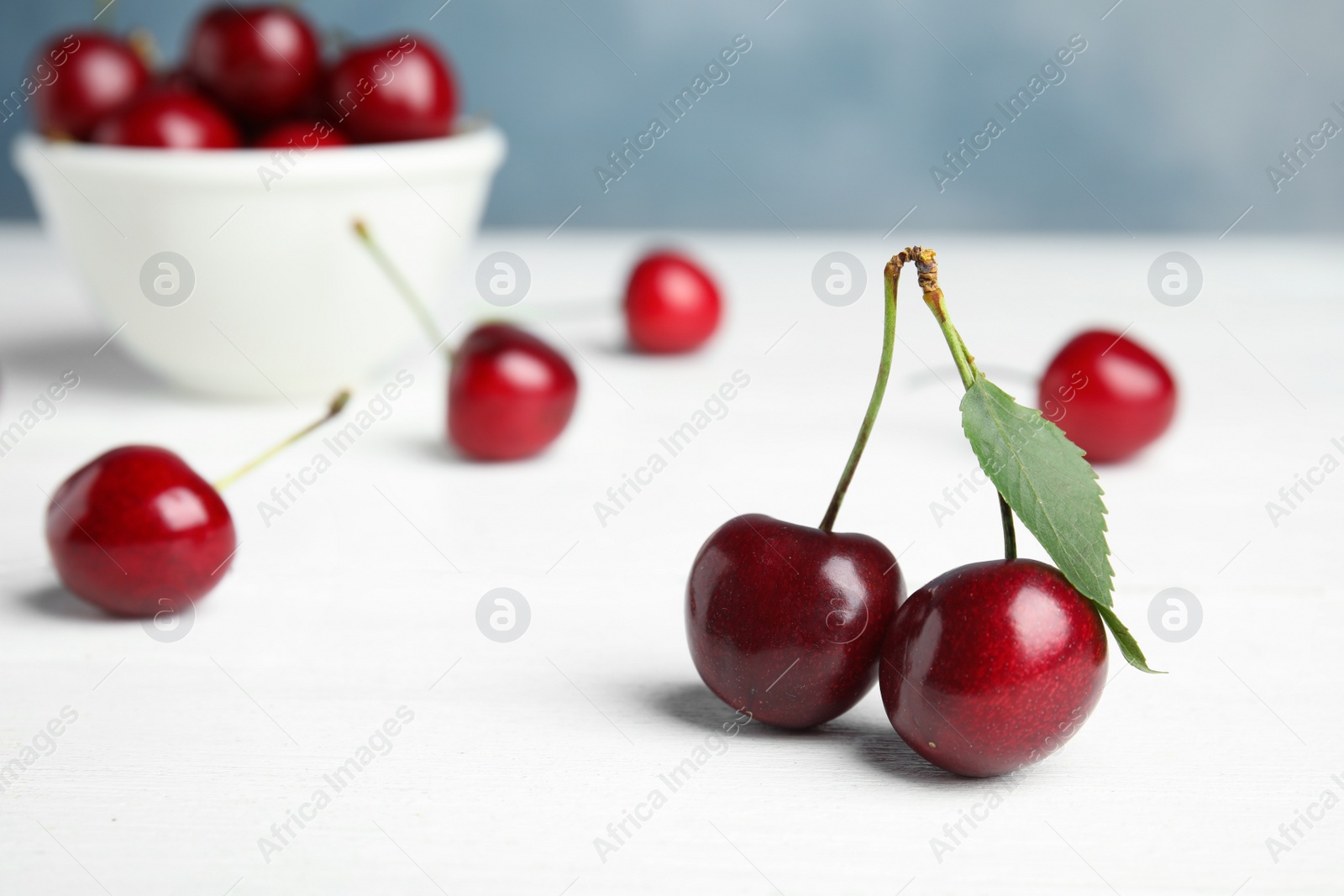 Photo of Ripe sweet cherries on white wooden table. Space for text