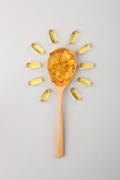Photo of Wooden spoon with vitamin capsules on light background, top view