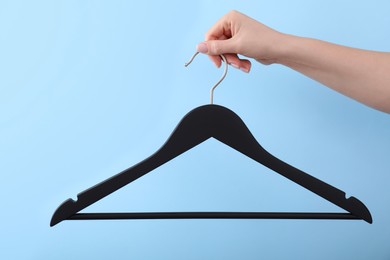 Woman holding hanger on light blue background, closeup