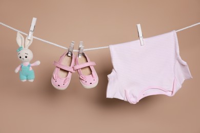 Photo of Cute small baby shoes, tshirt and toy hanging on washing line against brown background