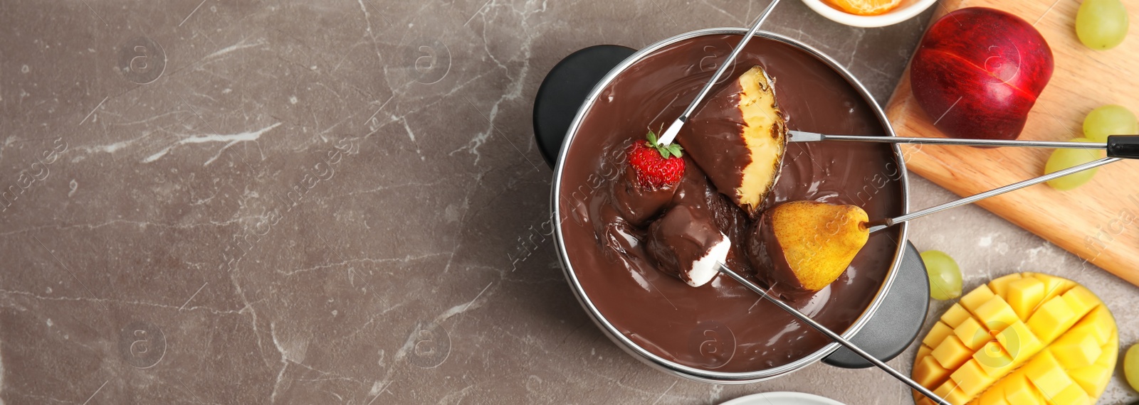 Image of Flat lay composition with chocolate fondue in pot and fruits on brown marble table, space for text. Banner design