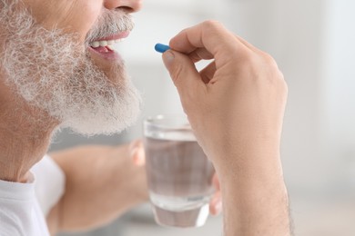 Photo of Senior man with glass of water taking pill on blurred background, closeup