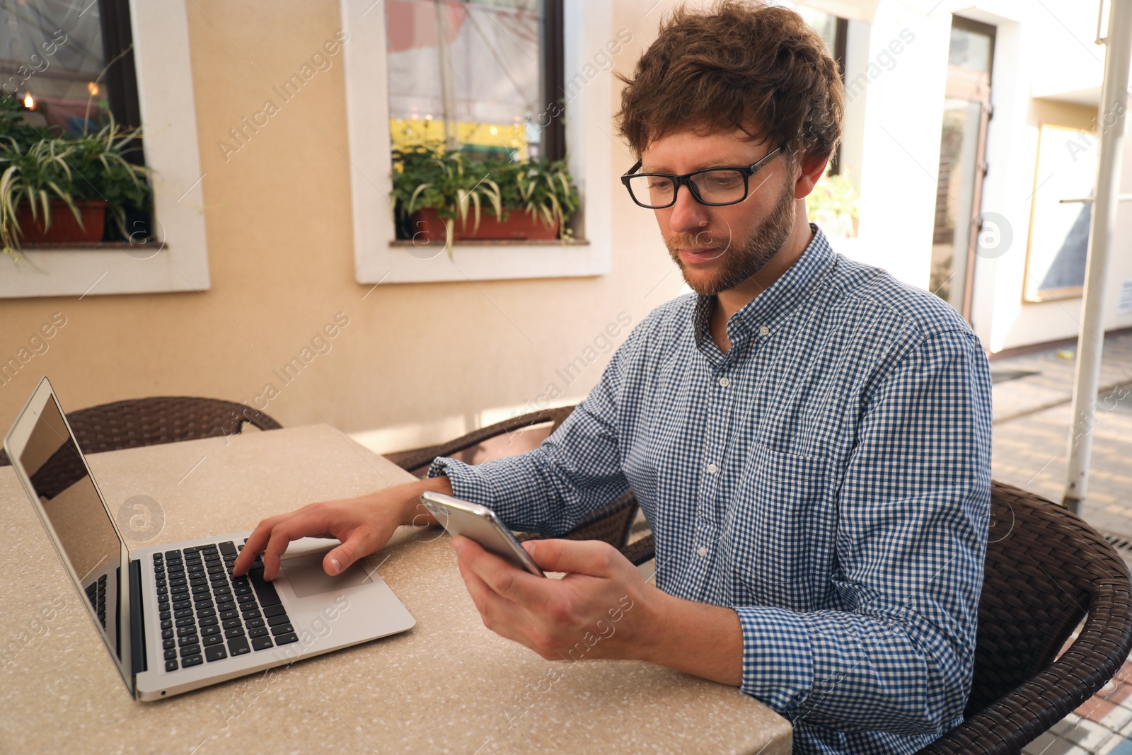 Photo of Handsome man using smartphone and laptop at table in cafe