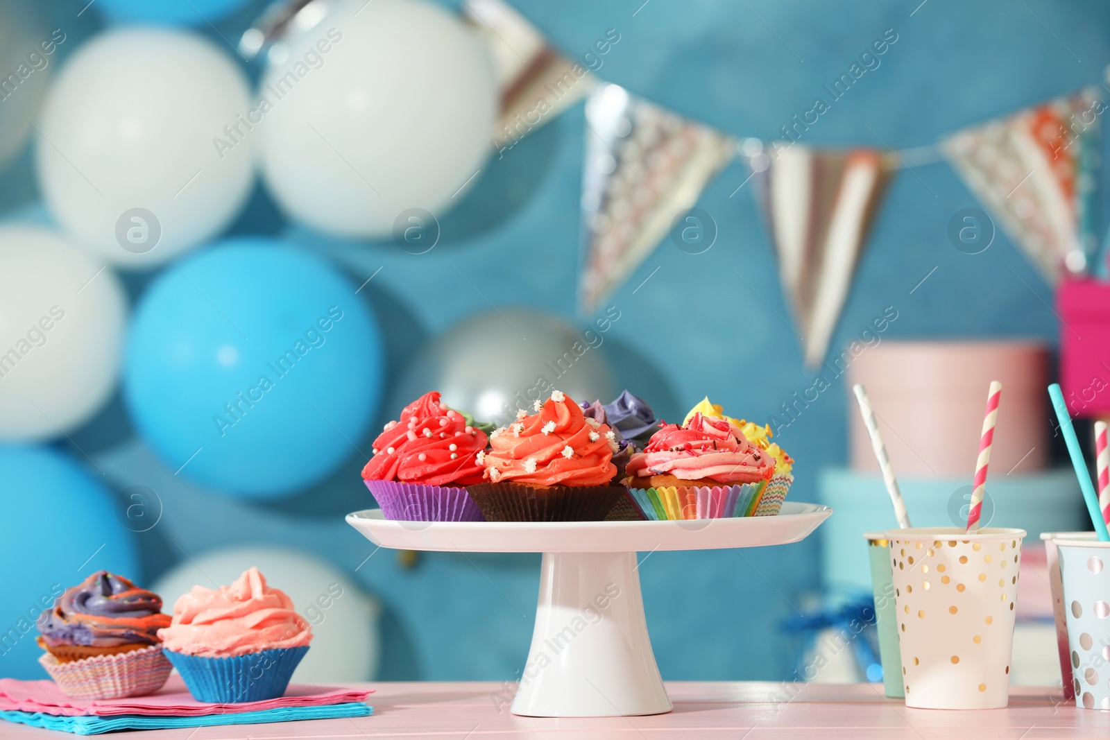 Photo of Different colorful cupcakes and party accessories on pink table