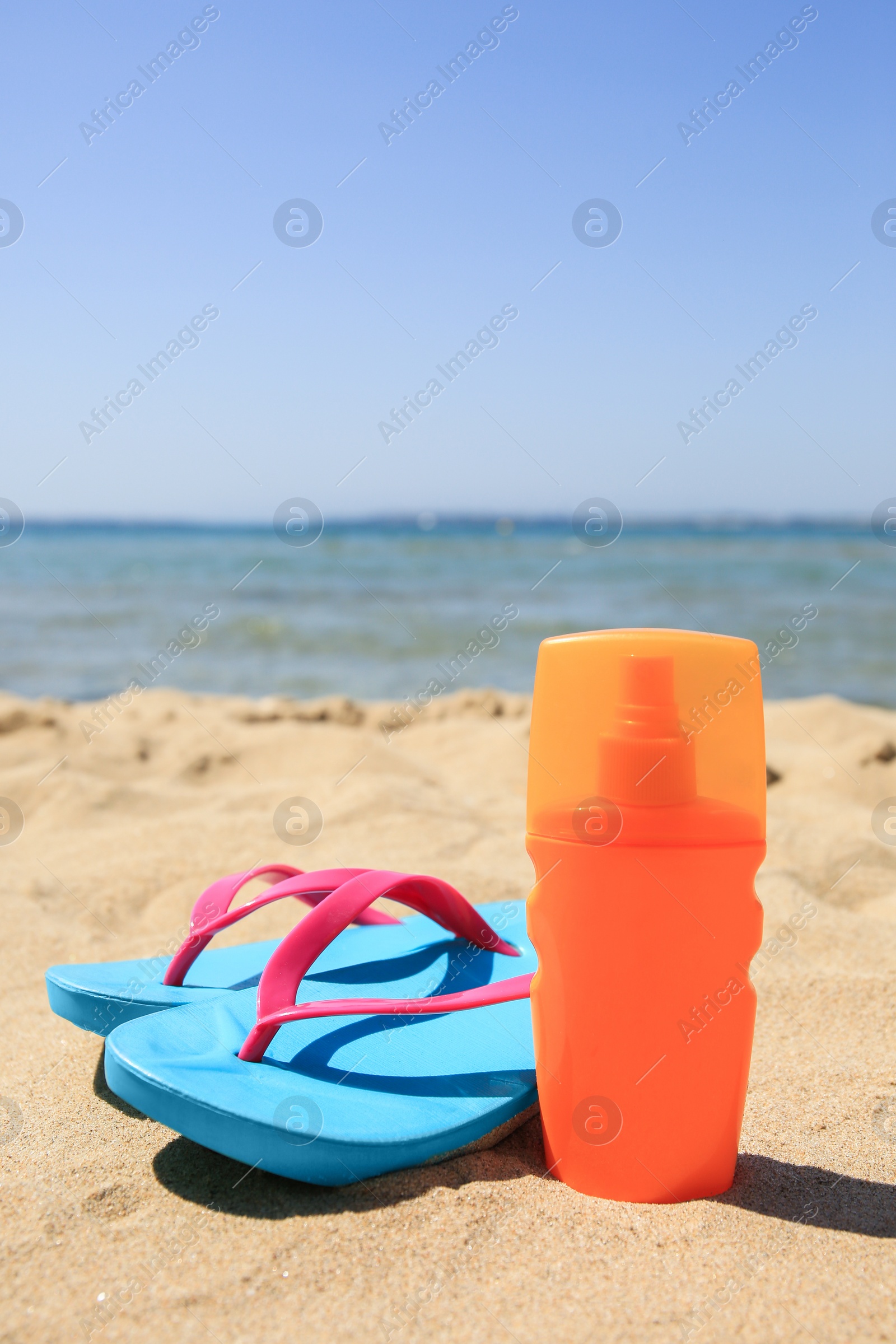 Photo of Sunscreen and flip flops on sandy beach. Sun protection care