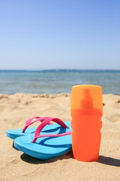 Sunscreen and flip flops on sandy beach. Sun protection care