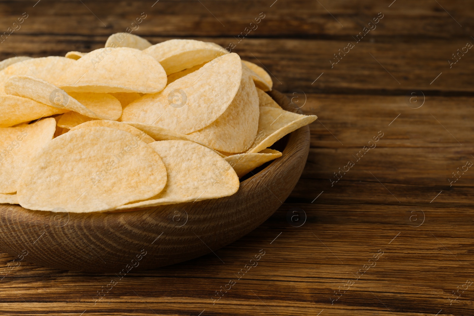 Photo of Bowl with delicious potato chips on wooden table, closeup. Space for text