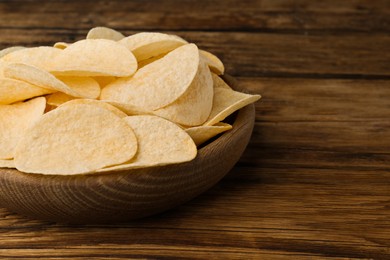 Bowl with delicious potato chips on wooden table, closeup. Space for text