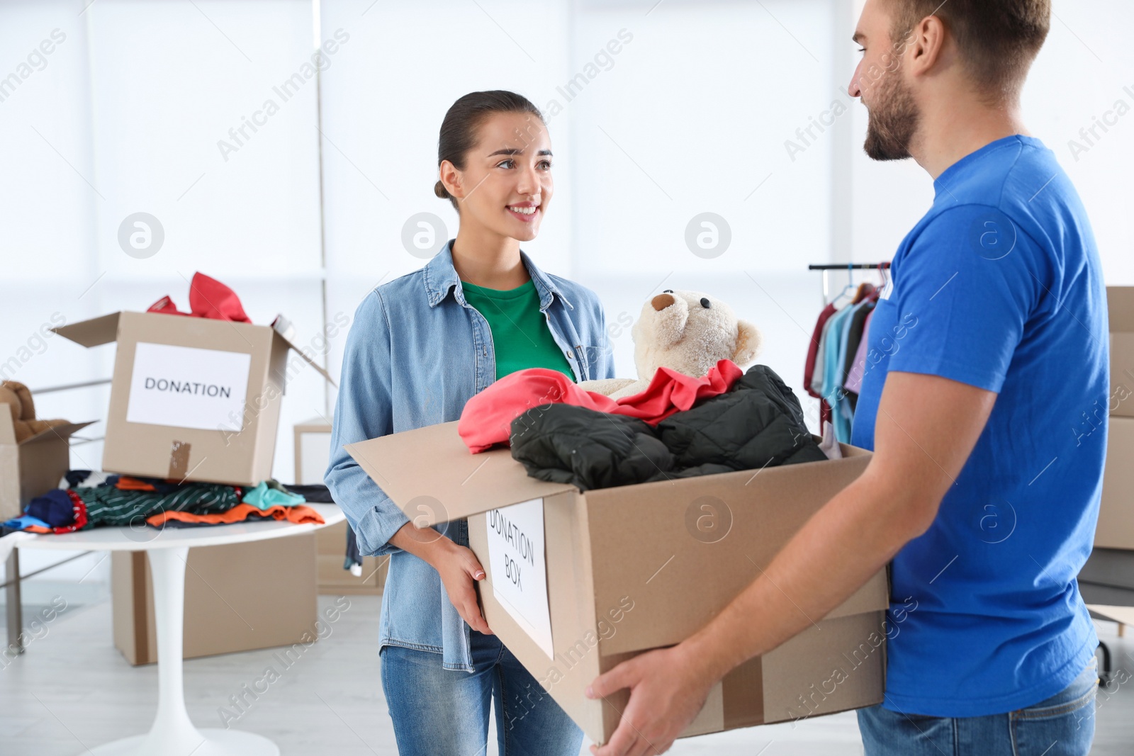 Photo of Young woman giving box with donations to male volunteer indoors