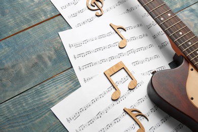 Guitar and sheets with music notes on wooden table. Space for text