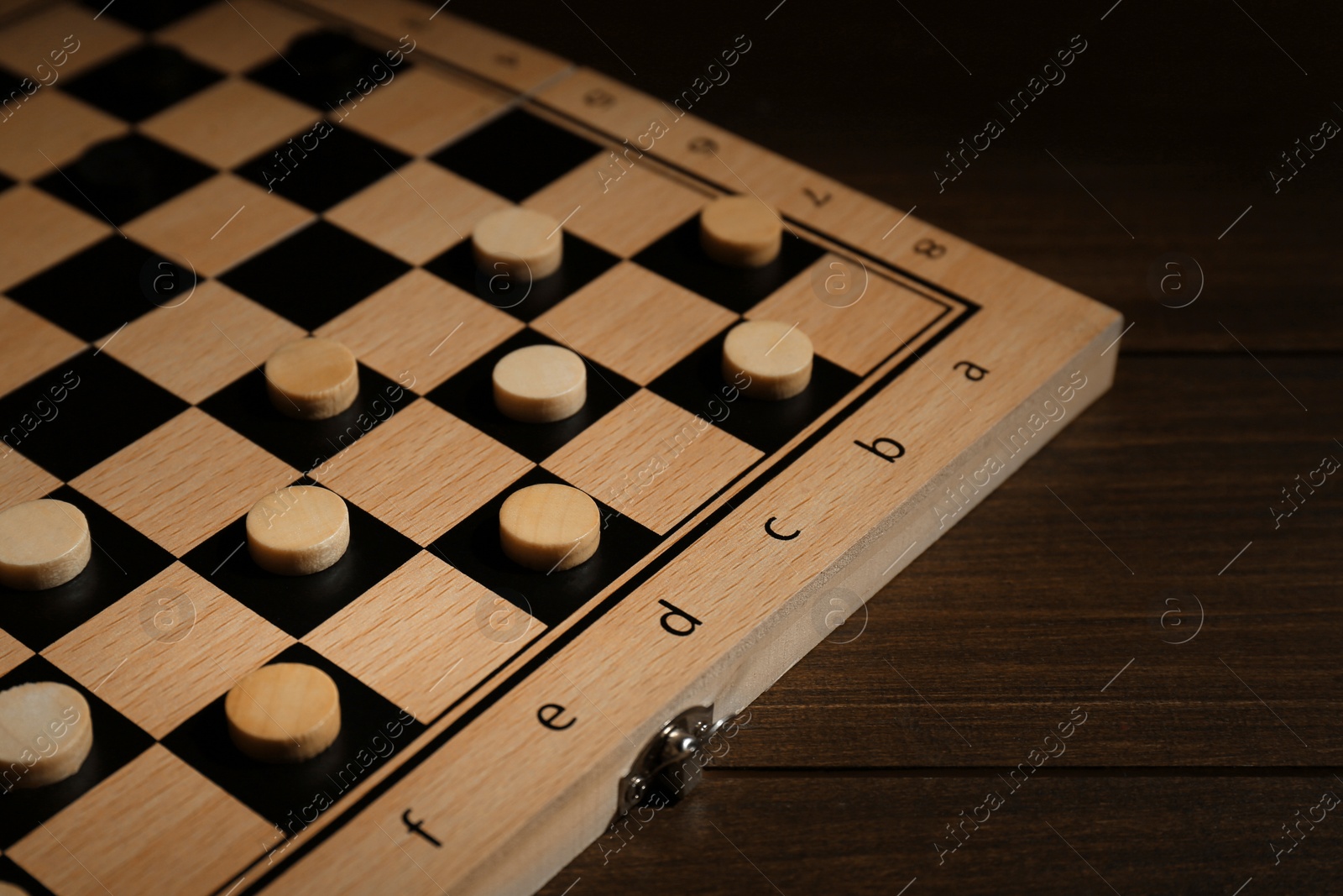 Photo of Checkerboard with game pieces on wooden table, closeup