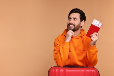 Photo of Smiling man with passport, suitcase and tickets on beige background. Space for text