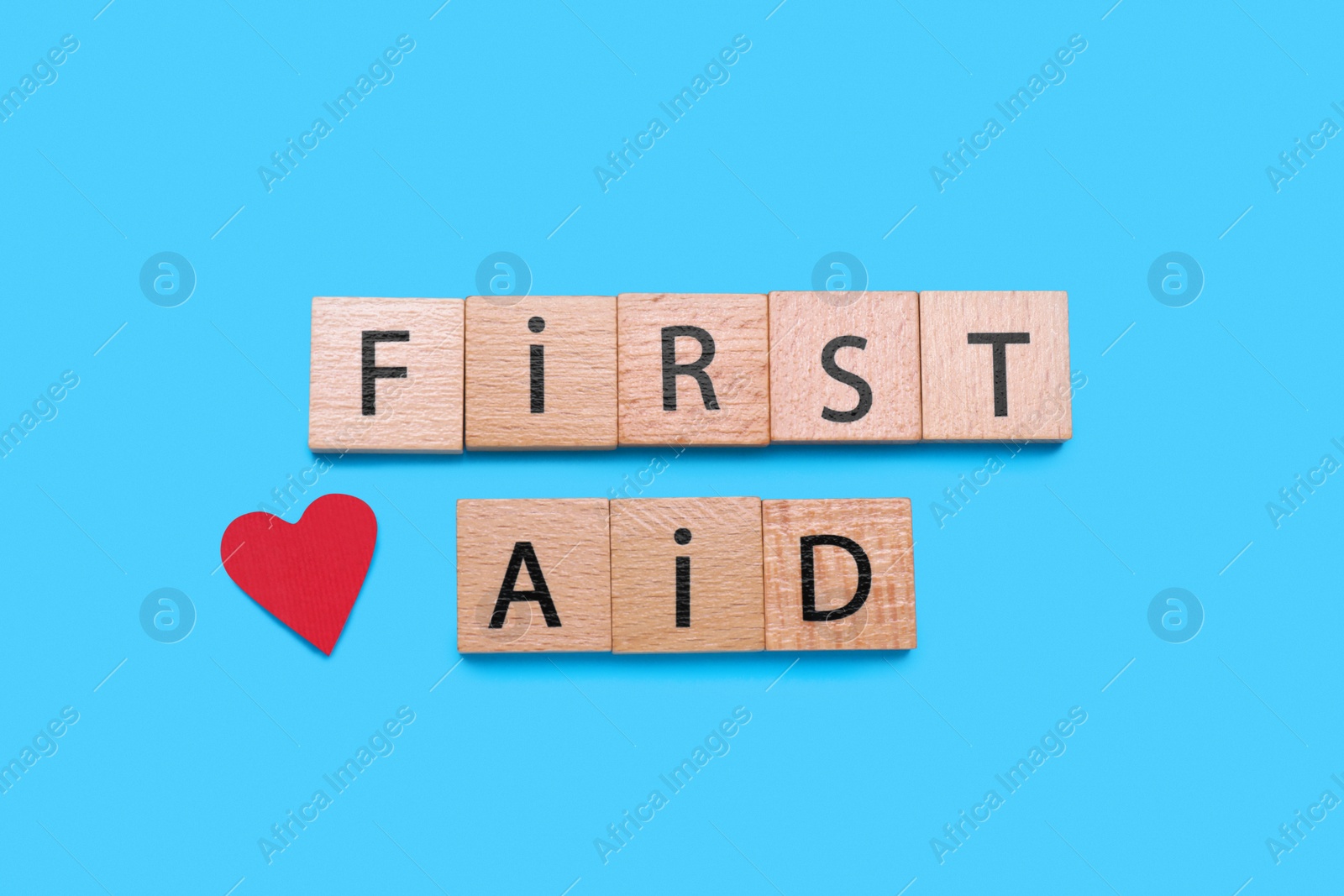 Photo of Words First Aid made of wooden cubes and cardboard heart on light blue background, flat lay