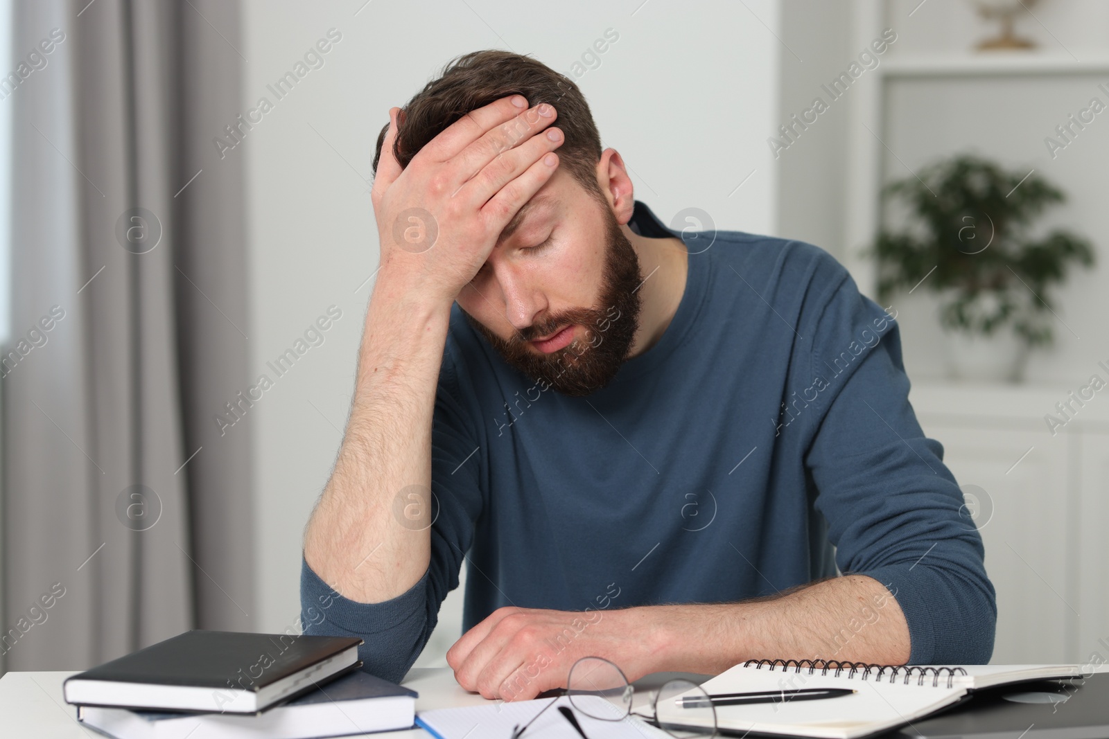 Photo of Overwhelmed man suffering from headache at table indoors