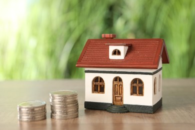 House model and stacked coins on wooden table outdoors