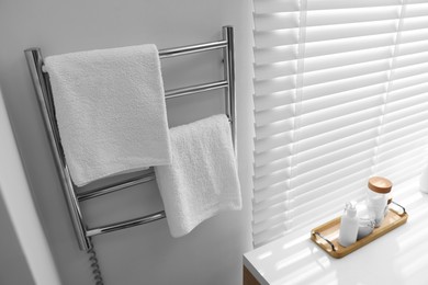 Photo of Heated rail with towels on white wall in bathroom