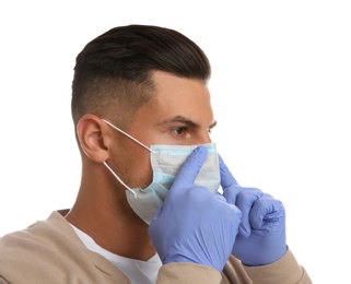Man in medical gloves putting on protective face mask against white background