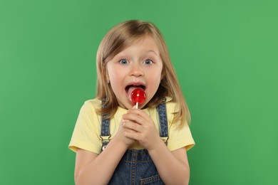Photo of Portrait of cute girl licking lollipop on green background