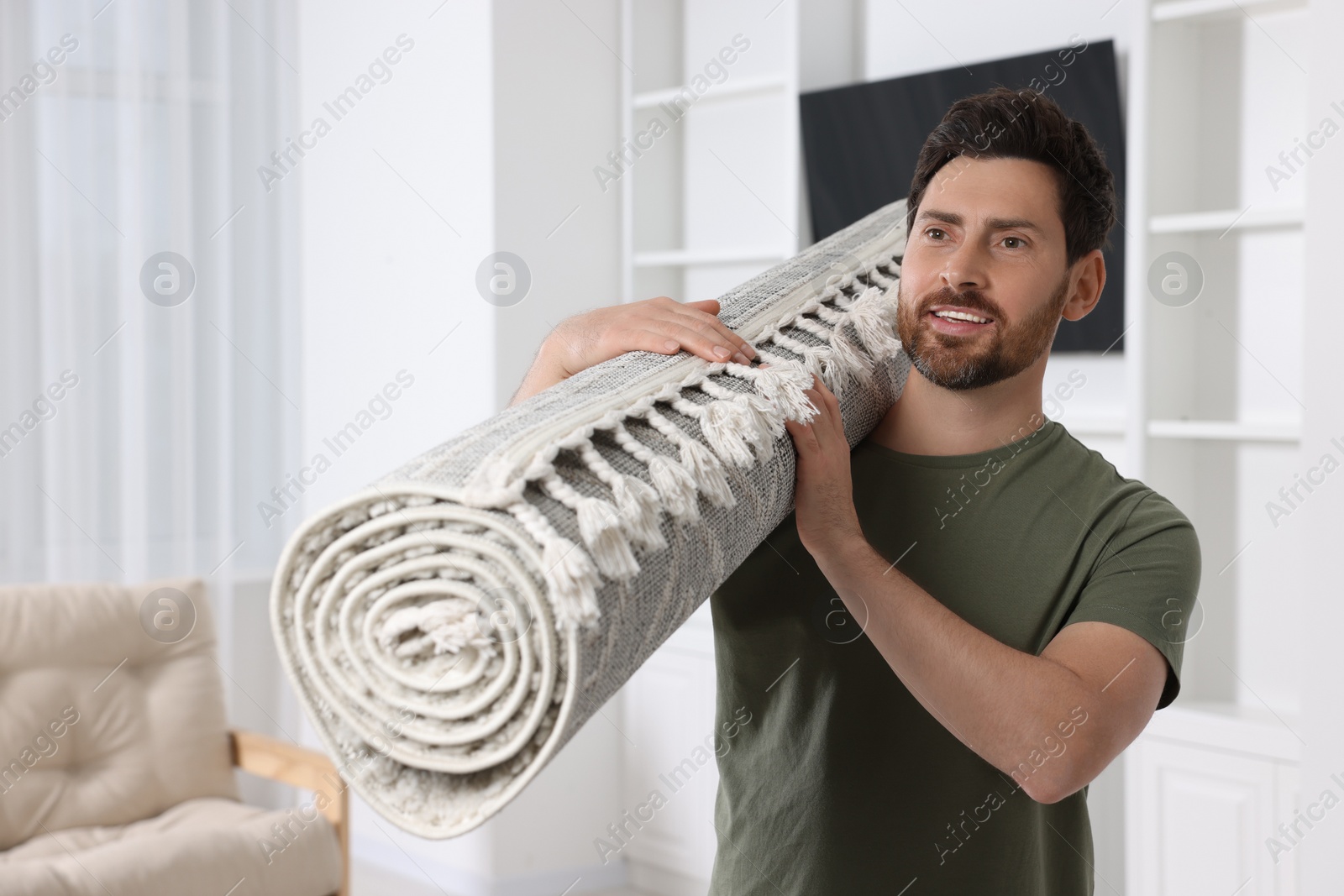 Photo of Smiling man holding rolled carpet in room