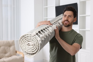 Photo of Smiling man holding rolled carpet in room