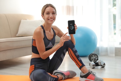Young woman showing smartphone with fitness app at home