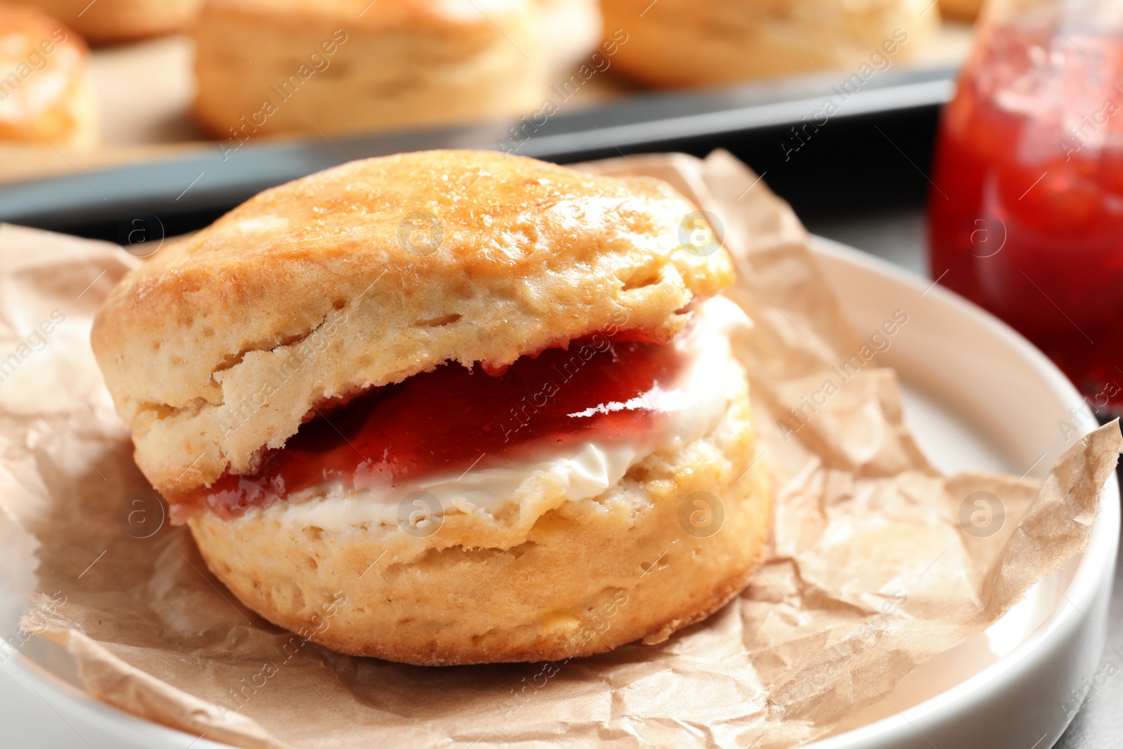 Photo of Tasty scone with clotted cream and jam on plate, closeup