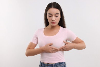 Beautiful young woman doing breast self-examination on white background