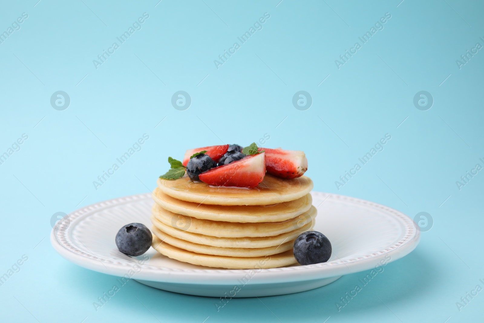 Photo of Delicious pancakes with strawberries, blueberries and mint on light blue background