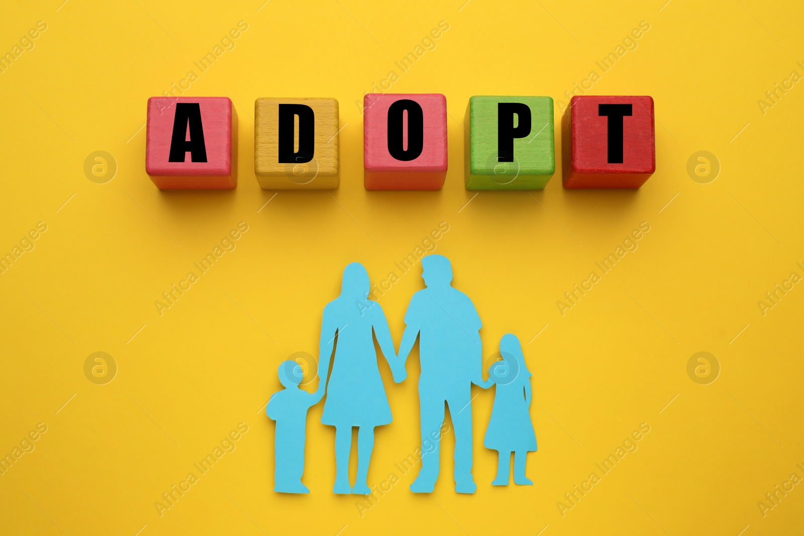 Photo of Family figure and word Adopt made of cubes on yellow background, flat lay