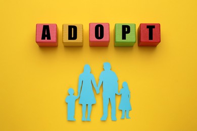 Photo of Family figure and word Adopt made of cubes on yellow background, flat lay