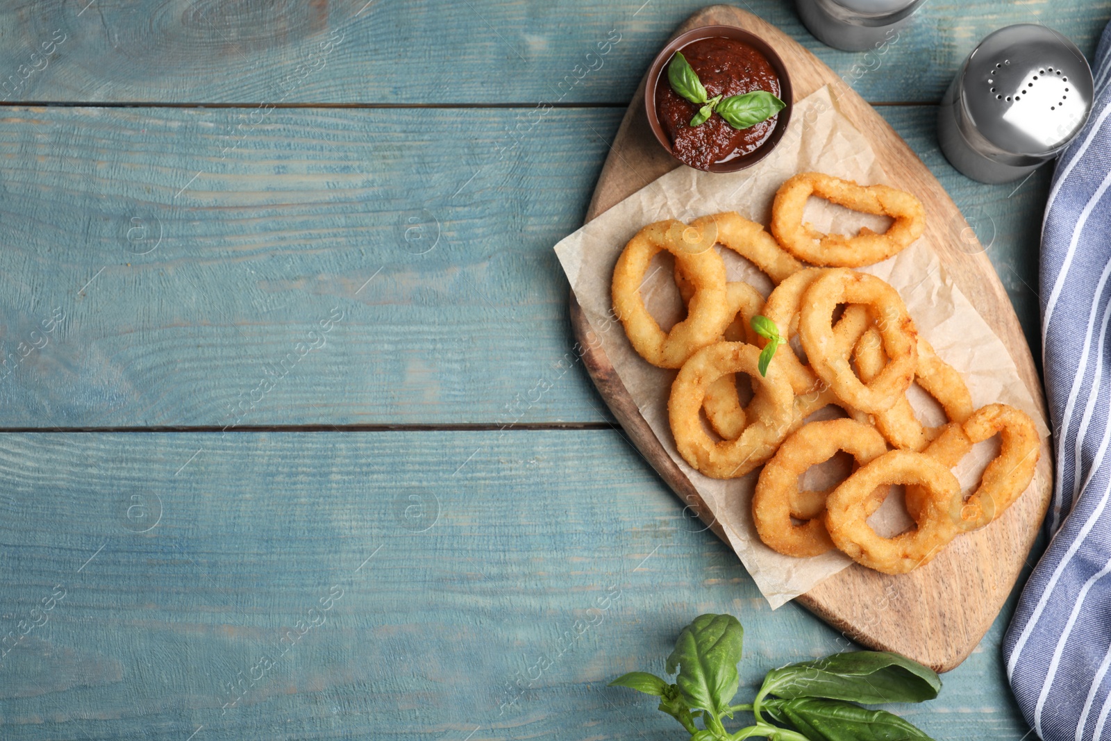 Photo of Fried onion rings served on blue wooden table, flat lay. Space for text