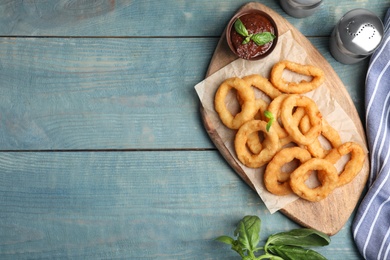 Photo of Fried onion rings served on blue wooden table, flat lay. Space for text