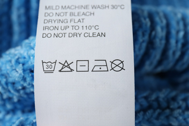 Photo of Clothing label with care symbols on blue sweater, closeup view