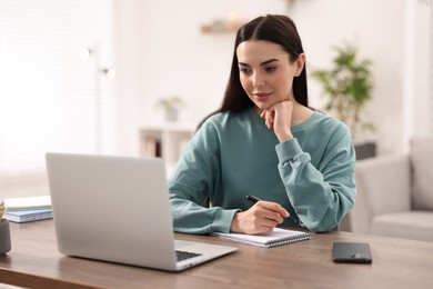 Young woman watching webinar at table in room